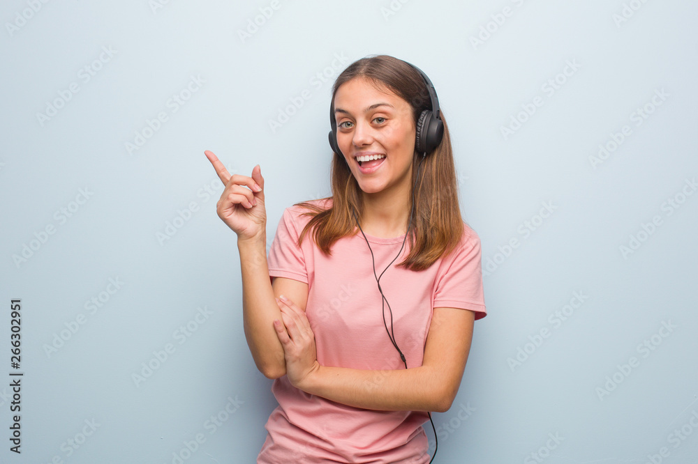 Young pretty caucasian woman pointing to the side with finger. She is listening to music with headphones. Young pretty caucasian woman pointing to the side with finger. She is listening to music with headphones.