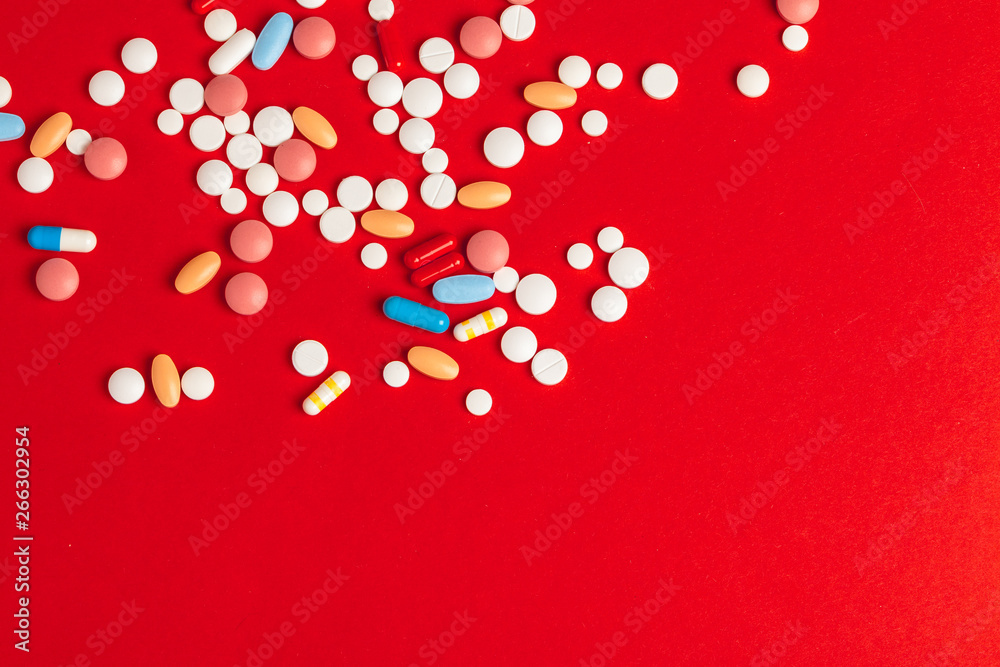 White pills spilling out of a toppled white bottle on red background