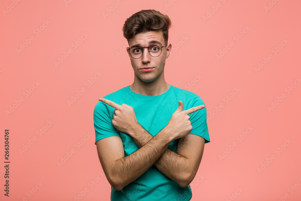 Young cool caucasian man points sideways, is trying to choose between two options.