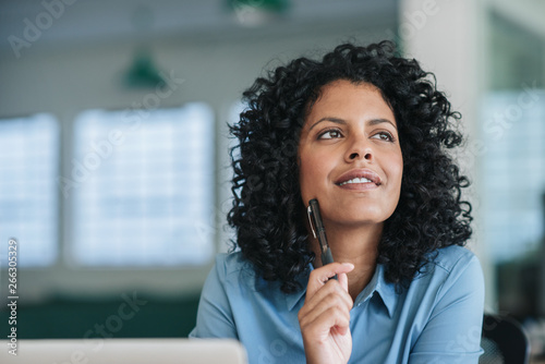 Smiling young businesswoman deep in thought at her office desk