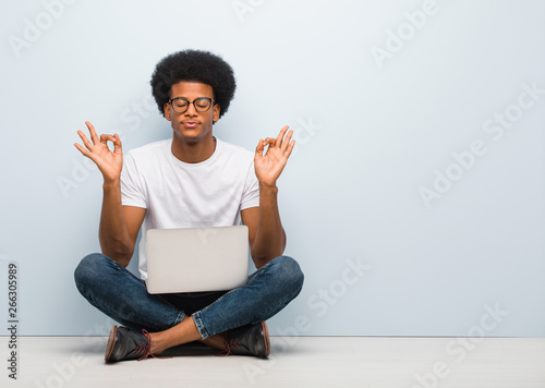 Young black man sitting on the floor with a laptop performing yoga