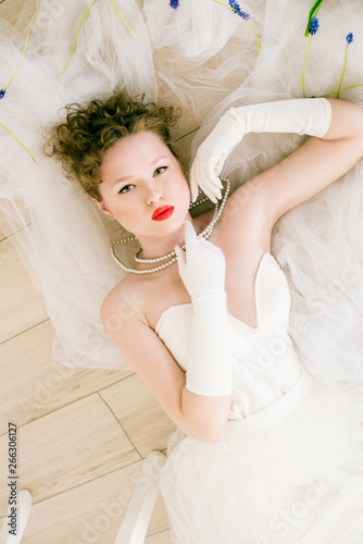 Young beautiful bride in a white dress in the style of the 80s with red lipstick on her lips lying on the floor in tulips photo