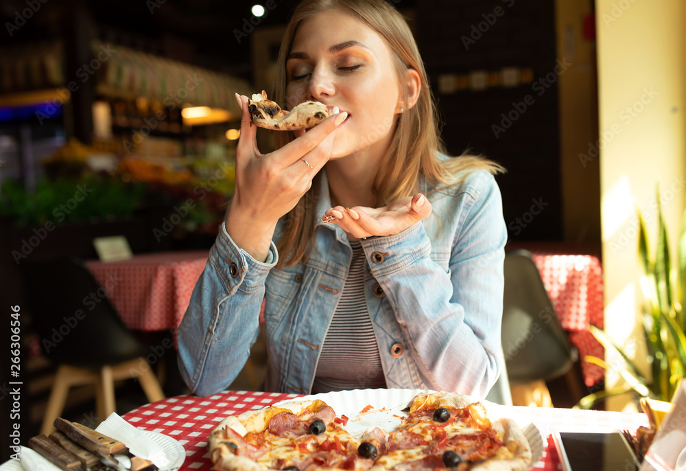 Funny blonde girl in jeans jacket eating pizza at restaurant. Stock Photo |  Adobe Stock