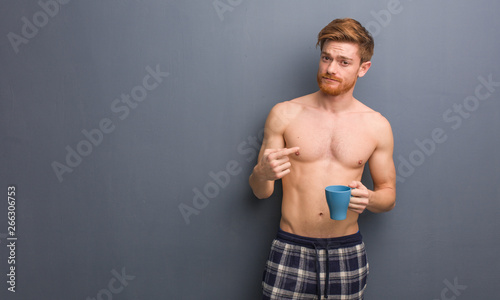 Young shirtless redhead man inviting to come. He is holding a coffee mug.