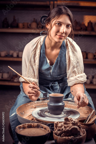 Stylish young and cheerful woman working on potter's wheel with raw clay with hands. Making ceramic dishes.