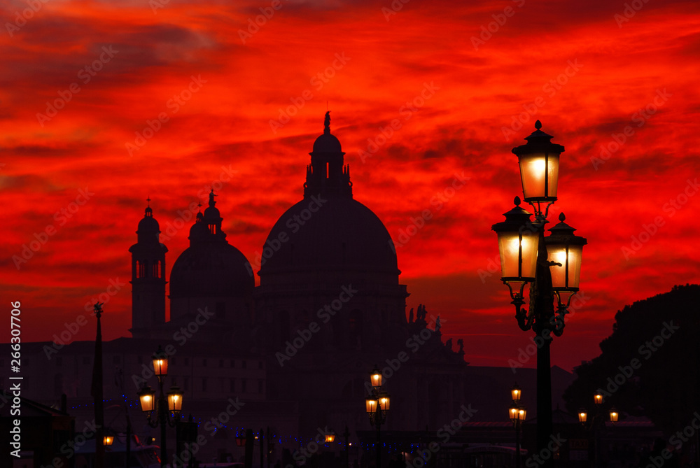 Mysterious blood red sunset over Salute Basilica (Saint Mary of Health) domes with old street lamps in Venice