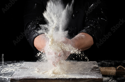 chef in black uniform sprinkles white wheat flour over the table