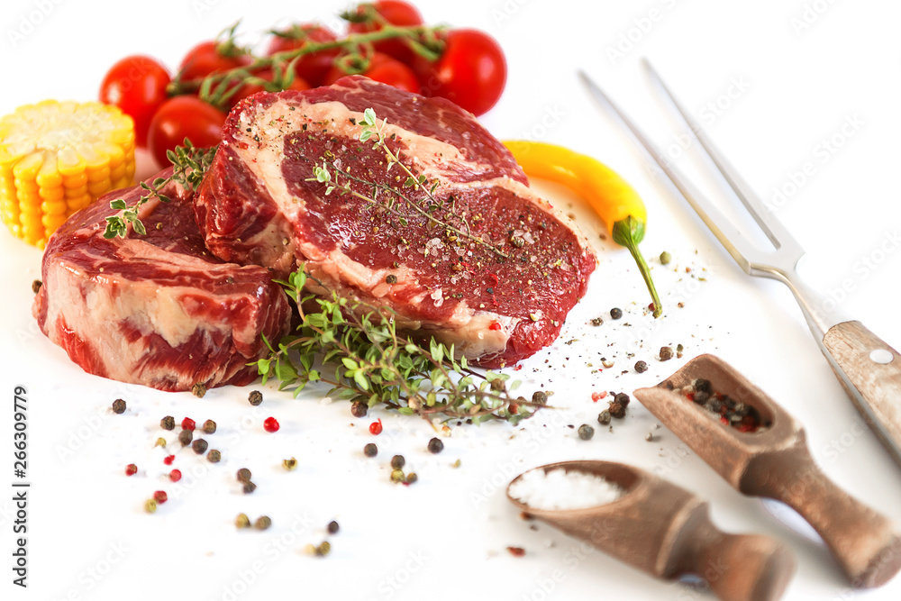 set for cooking a festive dinner for two. two raw marbled beef steaks, spices, vegetables and a grill pan with a meat fork. all on a white background