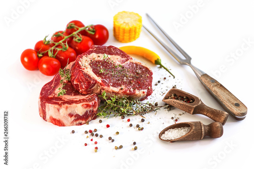 set for cooking a festive dinner for two. two raw marbled beef steaks, spices, vegetables and a grill pan with a meat fork. all on a white background