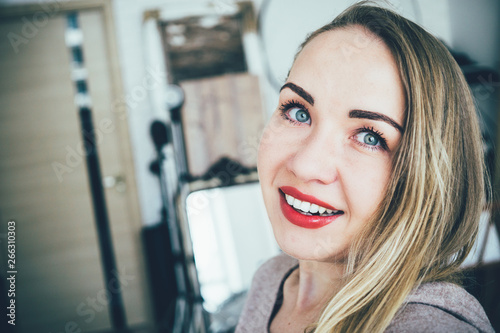 Smiling young european blonde woman making selfie in her studio apartment