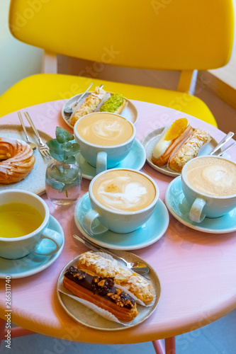 Cafe table with cups of coffee, eclairs and cake