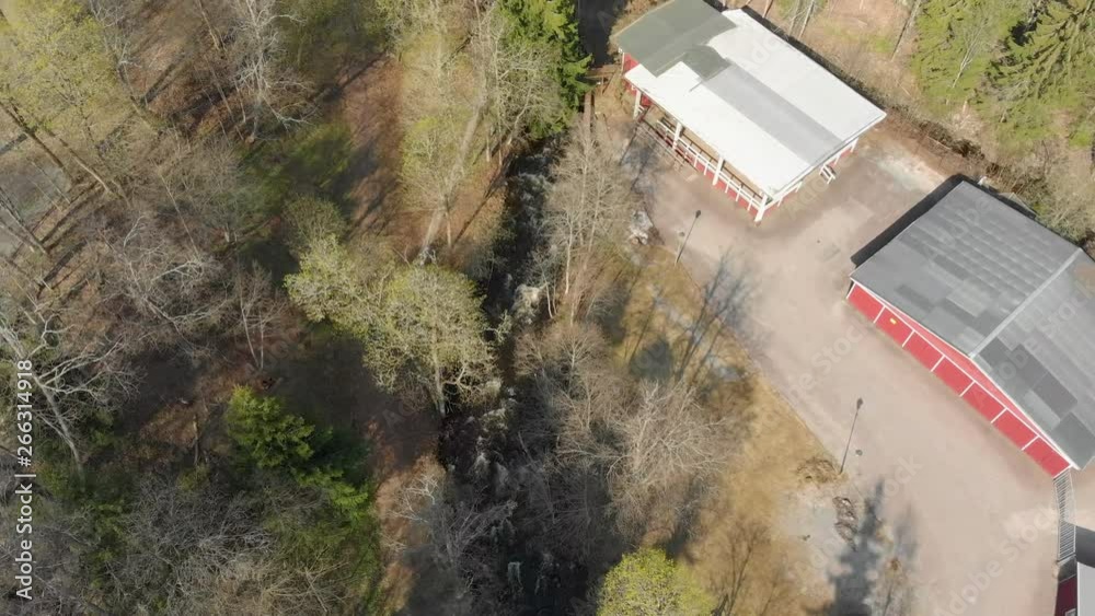 Drone footage flying high above a fast flowing stream of white foamed water with trees and a building in sight. Filmed in realtime at 4K.