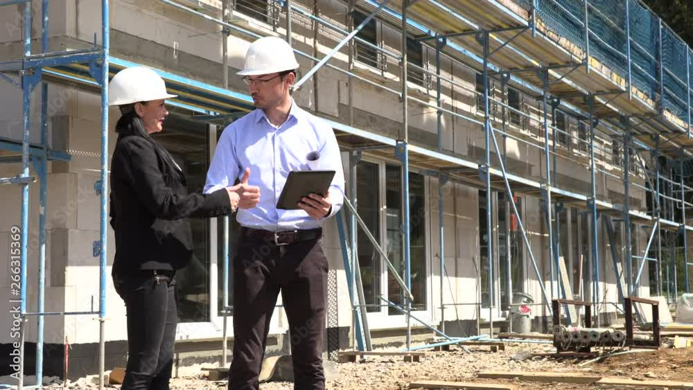Two architects in white helmets discuss a plan at a construction site Two architects in white helmets discuss a plan at a construction site