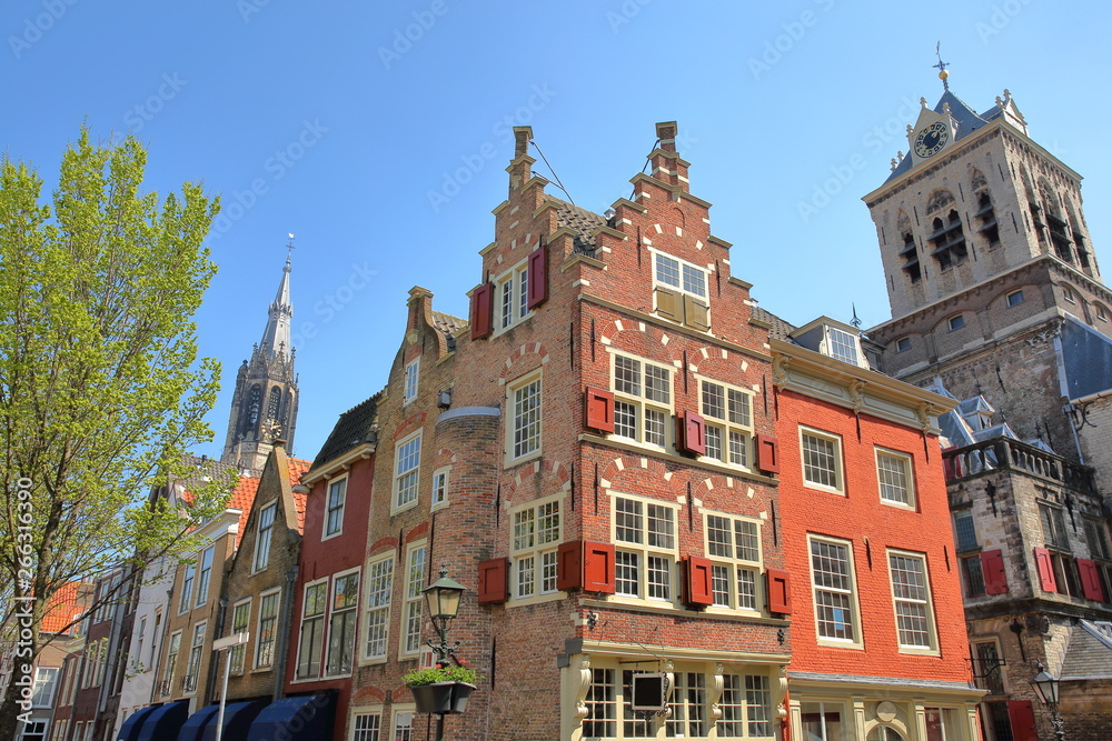 Traditional and colorful facades located at the junction of Markt and Voldersgracht street, with Nieuwe Kerk clock tower in the background and the Town Hall (Stadhuis) on the right, Delft, Netherlands