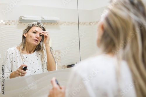 Woman applying morning make up in bathroom's mirror.