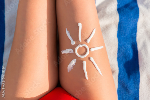 Woman sunbathing on the beach with a drawing of sun on her leg with sunscreen cream