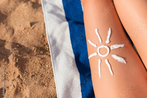 Sun cream is drawn in sun shape on tanned woman's leg who is relaxing on the towel at the beach. Cancer care concept