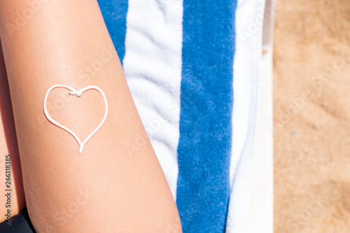 Sunscreen in the form of heart on woman's leg sunbathing on the towel by the sea