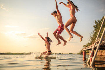 A group of young people joyfully leap into the refreshing lake waters on a sunny summer day, embracing the carefree moments of pure fun and laughter.