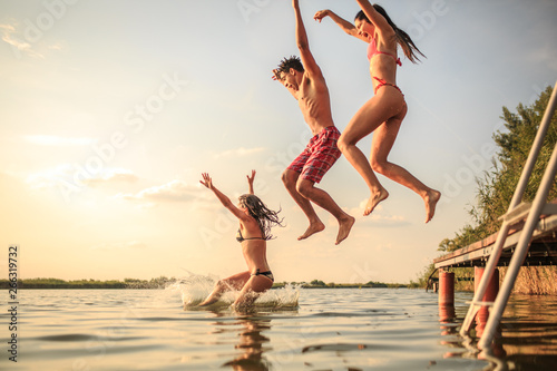 A group of young people joyfully leap into the refreshing lake waters on a sunny summer day, embracing the carefree moments of pure fun and laughter.
