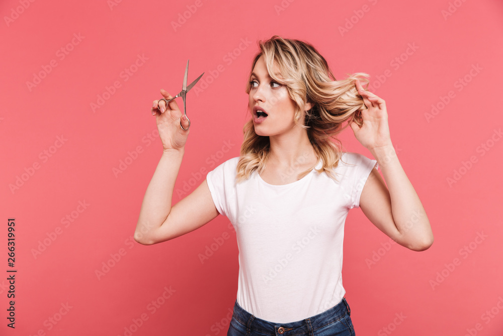 Portrait of puzzled blond woman 20s wearing casual t-shirt cutting her hair with scissors Portrait of puzzled blond woman 20s wearing casual t-shirt cutting her hair with scissors