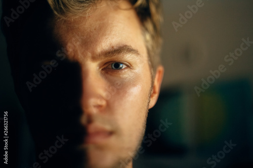 Serious man portrait in light on dark background. Closeup of man face with blue eyes and blonde hair in softlight. Selective focus. Creative image