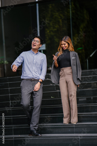 Full body Portrait of two professional businesspeople smiling and having a small talk while standing by the stairs of a building in Asia. The man and woman are both professionally dressed.