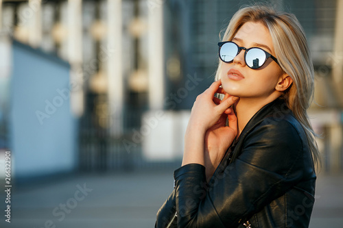 Lifestyle portrait of young pretty woman wearing mirror sunglasses and leather jacket. Empty space