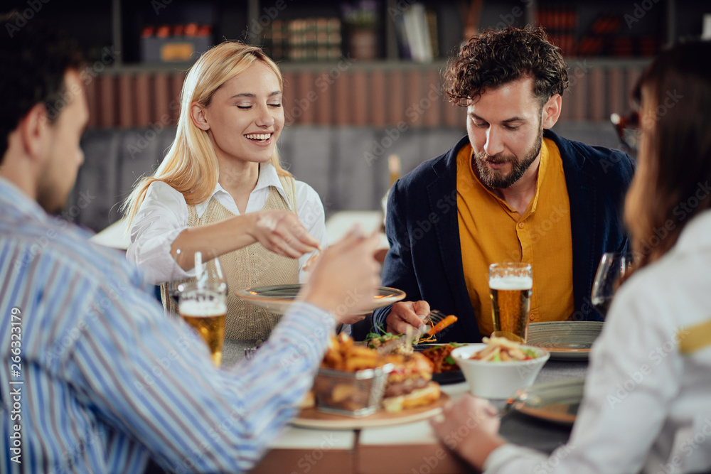 Multiethnic friends sitting at restaurant, drinking alcohol, chatting and having burgers for dinner.