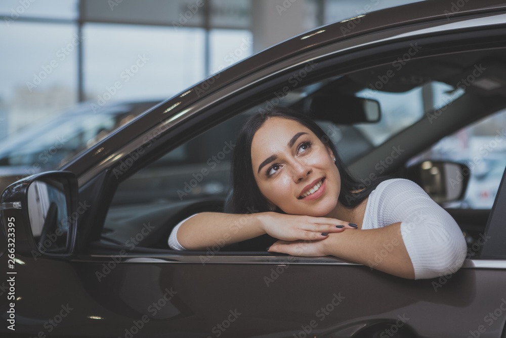 Happy beautiful dark haired woman buying new automobile at the dealership, sitting in a car looking away dreamily. Lovely female driver daydreaming of adventures, sitting in a new auto, copy space Happy beautiful dark haired woman buying new automobile at the dealership, sitting in a car looking away dreamily. Lovely female driver daydreaming of adventures, sitting in a new auto, copy space