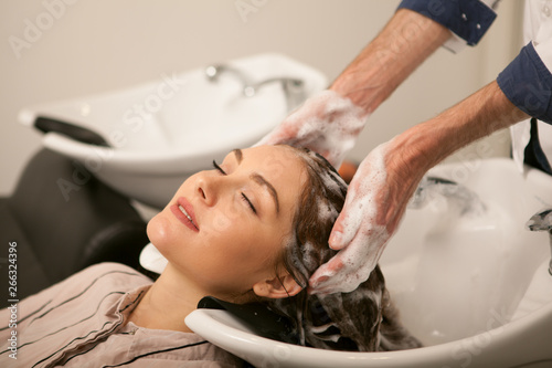 Cropped shot of the hands of professional hairdresser working at his beauty studio, washing hair of his female client. Beautiful woman enjoying head massage during hair wash at the salon, copy space