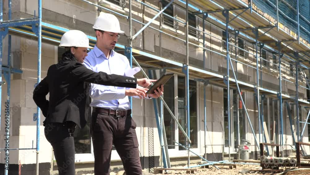 Two architects in white helmets discuss a plan at a construction site Two architects in white helmets discuss a plan at a construction site