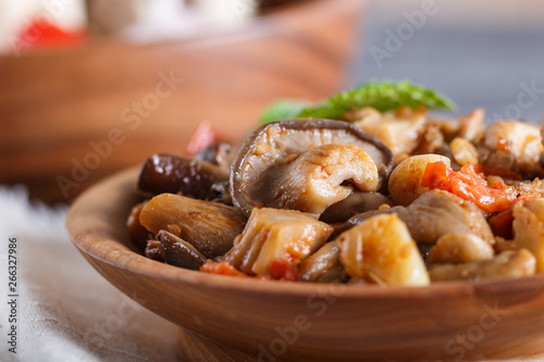 Fried oyster mushrooms with tomatoes in wooden plate on black concrete background. side view.