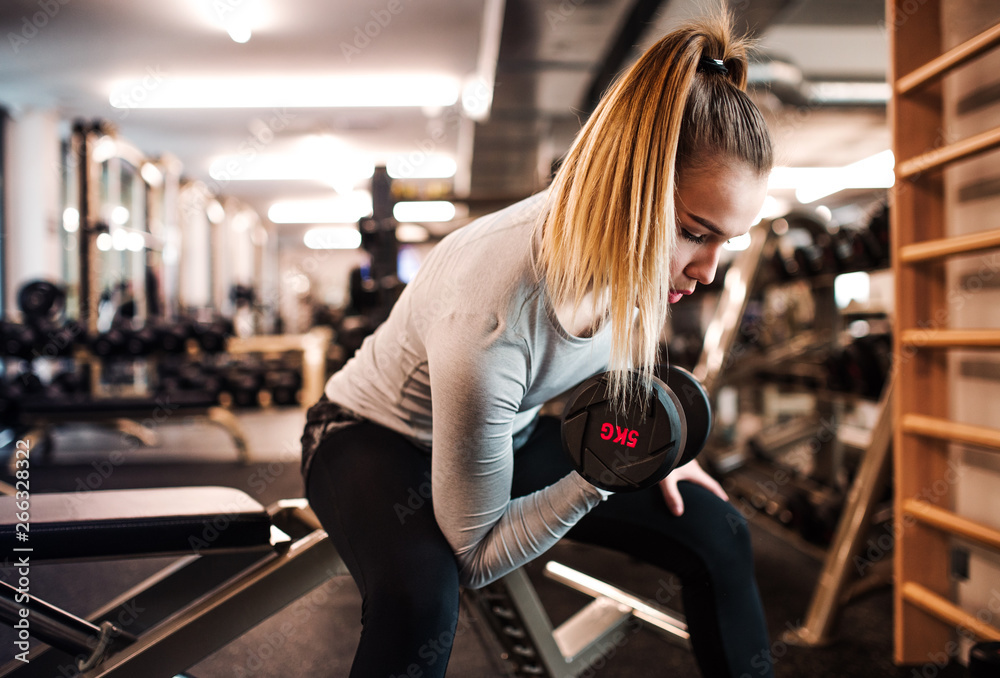 Fototapeta premium Young girl or woman with dumbbells, doing workout in a gym.