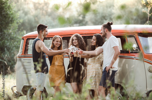 A group of friends standing outdoors on a roadtrip through countryside, clinking bottles. photo