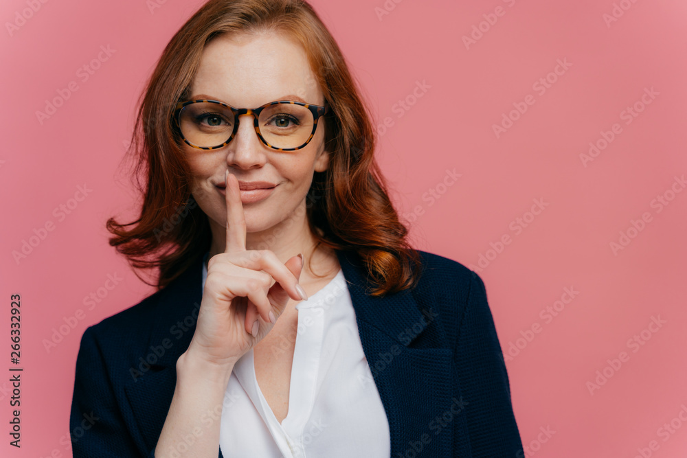 Isolated shot of attractive secret woman keeps fore finger over lips, demonstrates shush gesture, tells secret information, has healthy skin, manicure, makeup, wears formalwear, poses over pink wall Isolated shot of attractive secret woman keeps fore finger over lips, demonstrates shush gesture, tells secret information, has healthy skin, manicure, makeup, wears formalwear, poses over pink wall