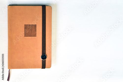 Notebook (beige, brown), lying on a white table, illuminated by natural muted daylight.
