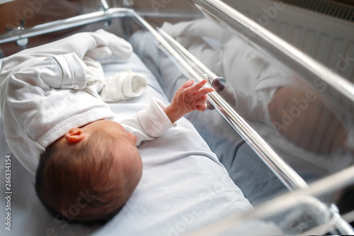 A newborn baby lies in a box in the hospital. Little baby shows his hand to the photographer. The hand of a newborn baby behind glass