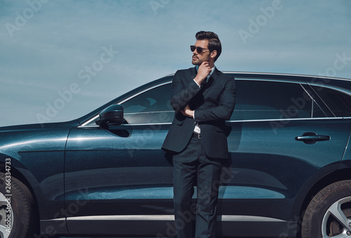 Confidence and charisma. Handsome young businessman keeping hand on chin while standing near his car outdoors © gstockstudio