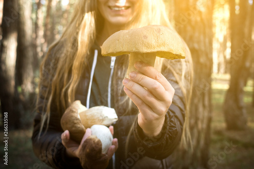 Boletus in the hand of a girl in the forest. Young smiling girl holds in her hand a boletus in the sunrise at the forest background.