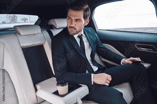 Confident businessman. Handsome young man in full suit looking away while sitting in the car photo