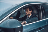 Just keep moving! Handsome young man in full suit looking straight while driving a car
