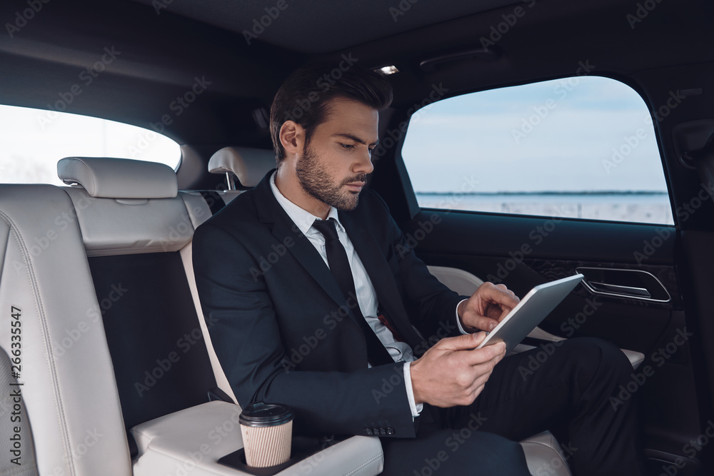 Considering the next step. Handsome young man in full suit working using digital tablet while sitting in the car