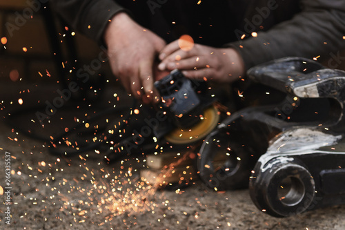Close up of male worker hand cutting metal pipe with electric grinder, orange sparks flying during working with steel at workshop. Dangerous work concept.