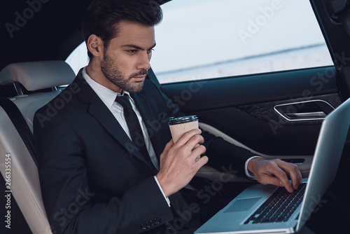 Working from car. Handsome young man in full suit working using laptop while sitting in the car © gstockstudio