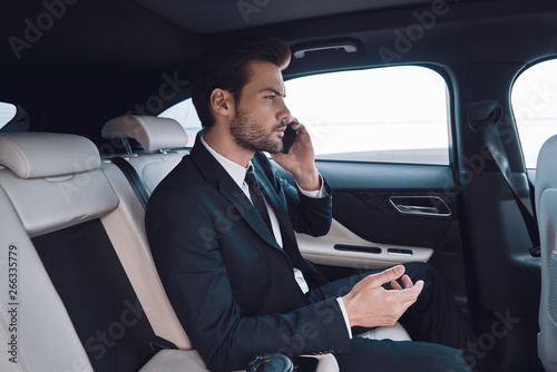 Always available. Handsome young man in full suit talking on the smart phone while sitting in the car © gstockstudio
