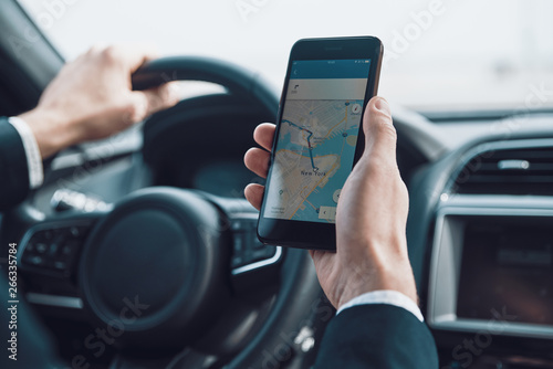 Searching for the shortest way. Close up of young man using smart phone to check the map while driving a car