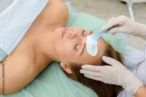 Face peeling mask, spa beauty treatment, skincare. Woman getting facial care by beautician at spa salon. Сosmetologist applying cream mask on face of a girl patient. Cosmetology. Close up