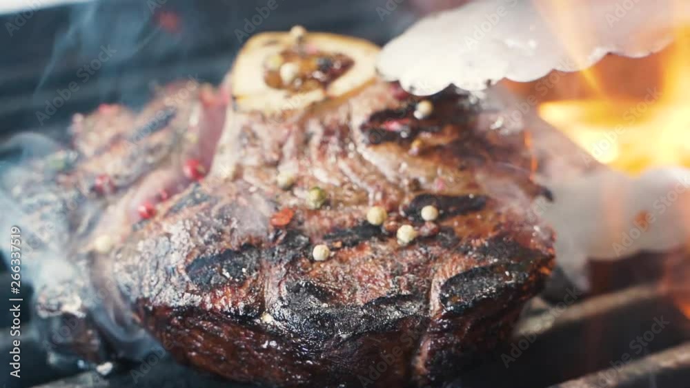 Chief using the spatula and turning the meat on the grill. Fire is burning, hot juicy oil steak cooking close up slow motion. Grill, tasty beefsteak slow motion Chief using the spatula and turning the meat on the grill. Fire is burning, hot juicy oil steak cooking close up slow motion. Grill, tasty beefsteak slow motion
