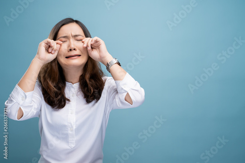 Sad woman crying and standing isolated on blue background